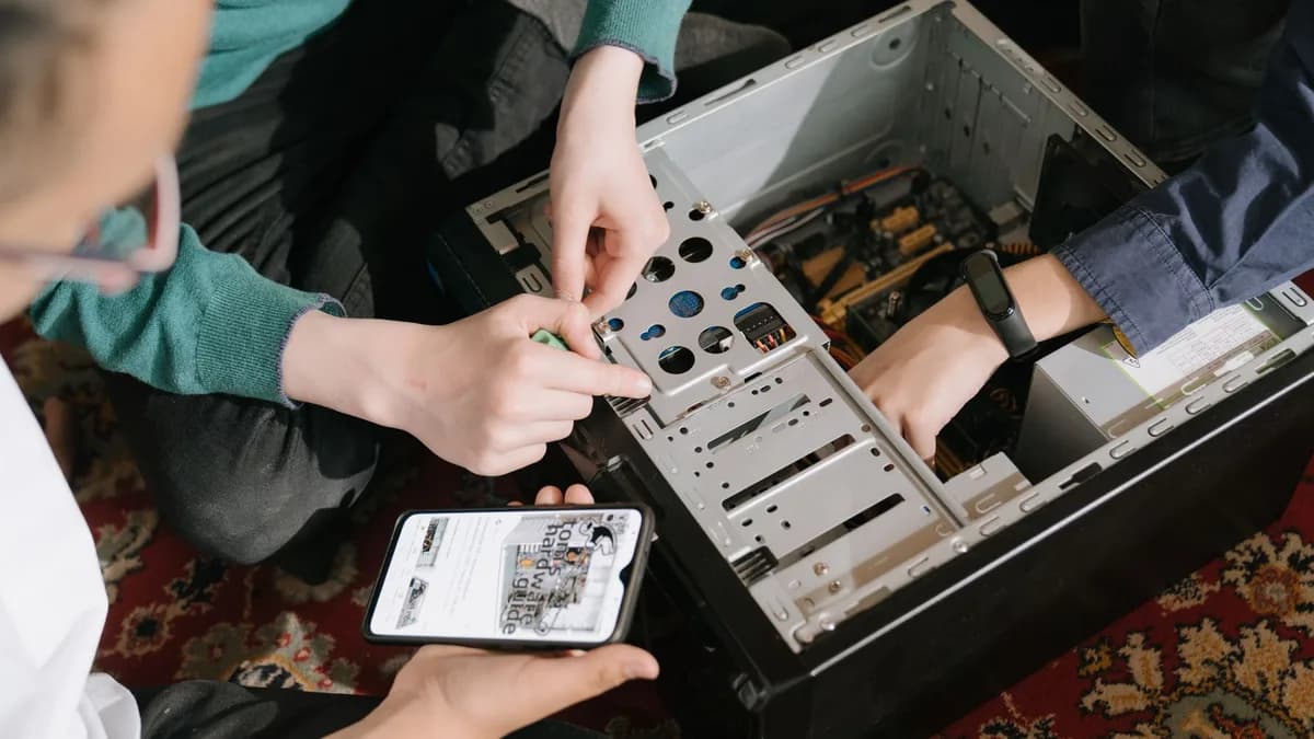 A close-up of hands fixing a computer with guidance from a mobile device.