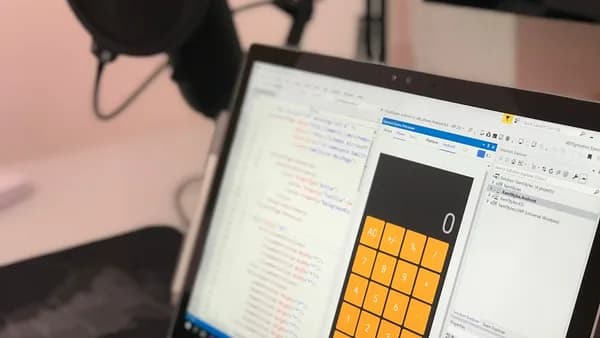 Close-up of a laptop displaying code and a calculator app in a modern workspace.