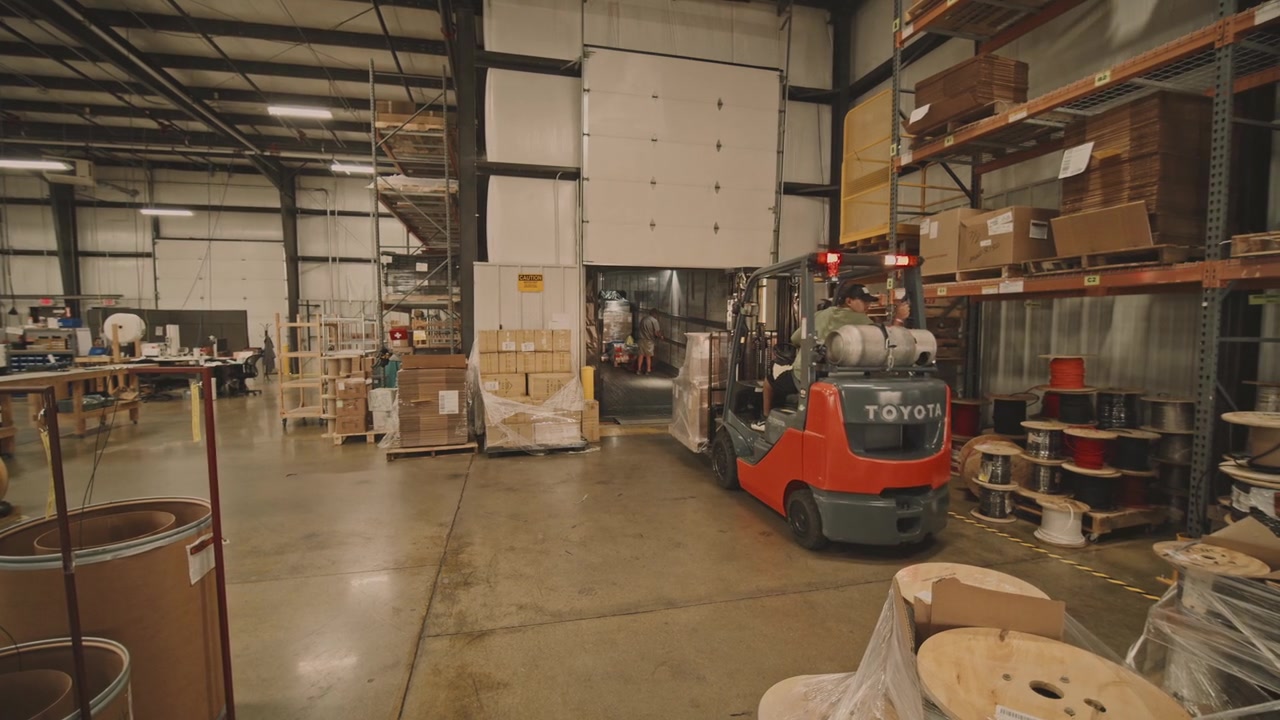 Warehouse footage frame at 5.4 seconds: an orange Toyota forklift with the operator visible, boxes stacked on wooden pallets